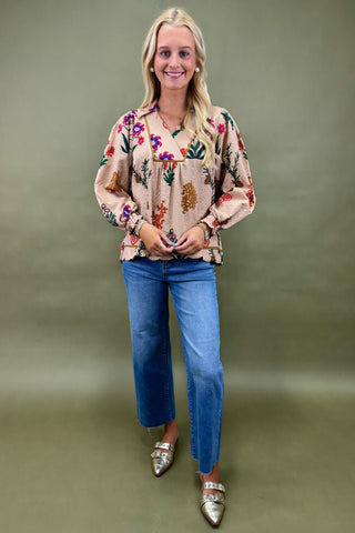 Woman wearing a floral blouse and blue jeans against a green background