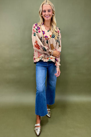 Woman wearing a floral blouse and blue jeans against a green background