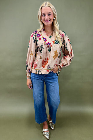 Woman wearing a floral blouse and blue jeans against a green background