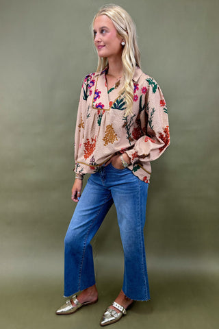 Woman wearing a floral blouse and blue jeans against a green background