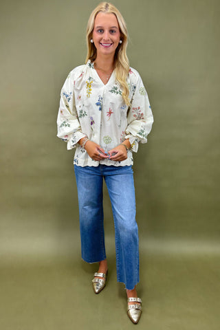 Woman wearing a floral blouse and blue jeans against a green background