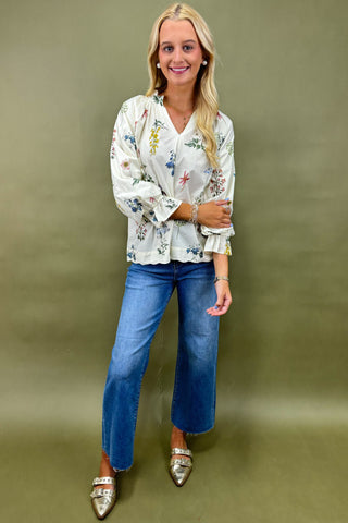 Woman wearing a floral blouse and blue jeans against a green background