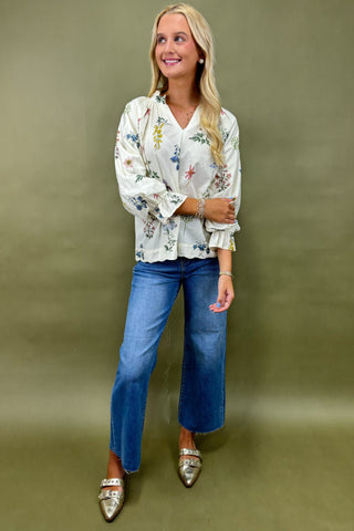 Woman wearing a floral blouse and blue jeans against a green background