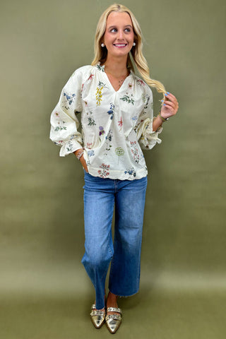 Woman wearing a floral blouse and blue jeans against a green background