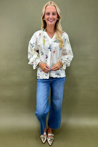Woman wearing a floral blouse and blue jeans against a plain background