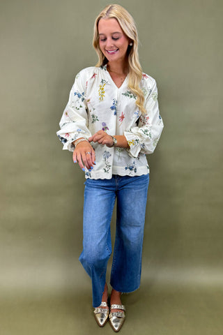 Woman wearing a floral blouse and blue jeans against a green background