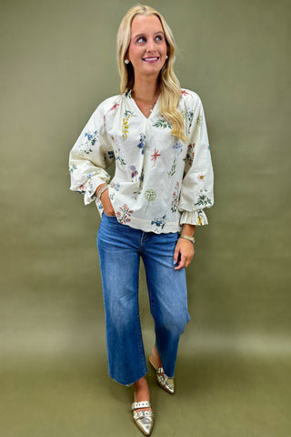 Woman wearing a floral blouse and blue jeans against a plain background