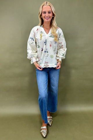 Woman wearing a floral blouse and blue jeans against a plain background