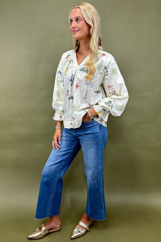 Woman wearing a floral blouse and blue jeans against a green background