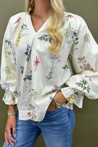 Woman wearing a white blouse with floral patterns and blue jeans against a green background