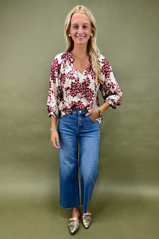 Woman wearing a floral blouse and blue jeans against a green background