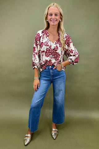 Woman wearing a floral blouse and blue jeans against a green background