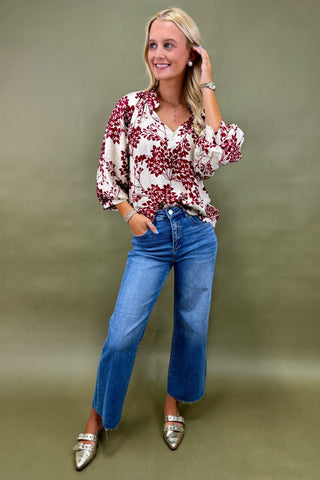 Woman wearing a floral blouse and blue jeans against a green background