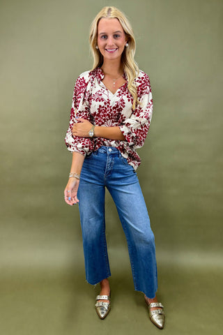 Woman wearing a floral blouse and blue jeans against a green background