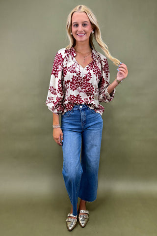 Woman wearing a floral blouse and blue jeans against a green background