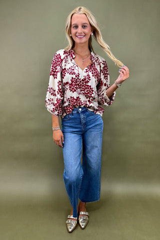 Woman wearing a floral blouse and blue jeans against a green background