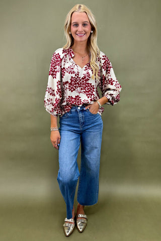 Woman wearing a floral blouse and blue jeans against a green background