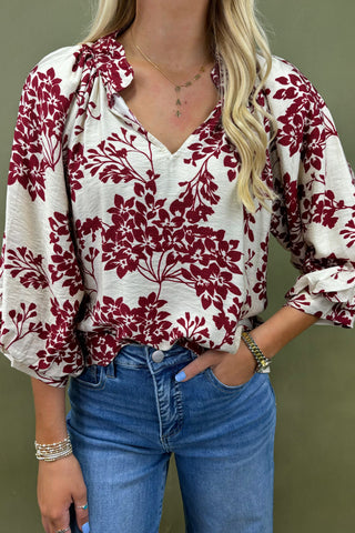 Woman wearing a red floral blouse and blue jeans against a green background