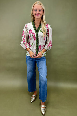Woman wearing a floral blouse, green shirt, blue jeans, and silver shoes on a green background