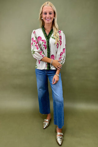 Woman wearing a floral embroidered jacket, green shirt, blue jeans, and silver shoes on a green background