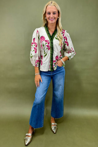 Woman wearing a floral blouse and blue jeans against a green background