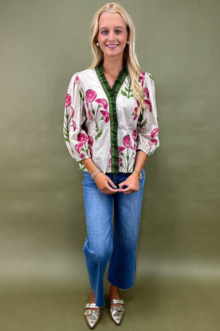 Woman wearing a floral blouse and blue jeans against a green background