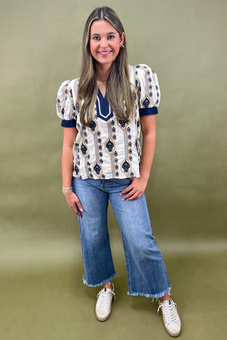 Cream and navy puff sleeve blouse with geometric print styled with light wash wide leg jeans and white sneakers.