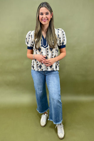 Cream and navy puff sleeve blouse with geometric print styled with light wash wide leg jeans and white sneakers.
