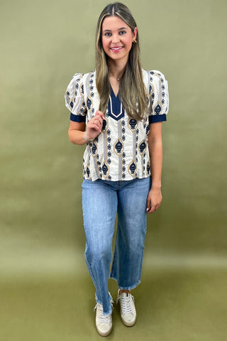 Cream and navy puff sleeve blouse with geometric print styled with light wash wide leg jeans and white sneakers.