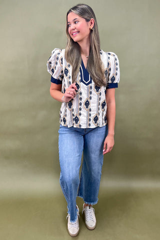 Cream and navy puff sleeve blouse with geometric print styled with light wash wide leg jeans and white sneakers.