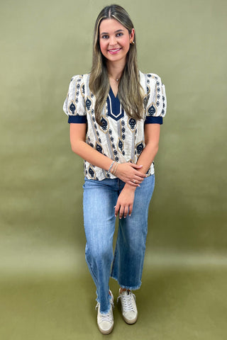 Cream and navy puff sleeve blouse with geometric print styled with light wash wide leg jeans and white sneakers.