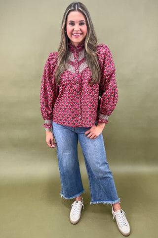 Woman wearing a red patterned blouse, blue jeans, and white sneakers on a green background