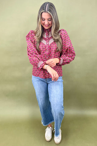 Woman wearing a pink patterned blouse and blue jeans against a green background