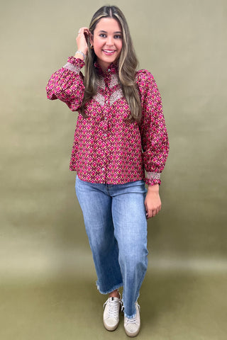 Woman wearing a patterned pink blouse and blue jeans against a plain background