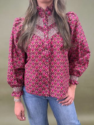 Woman wearing a red patterned blouse, blue jeans, and white sneakers on a green background