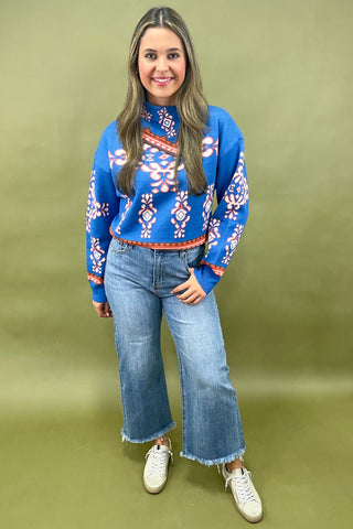Woman wearing a blue patterned sweater and jeans on a green background