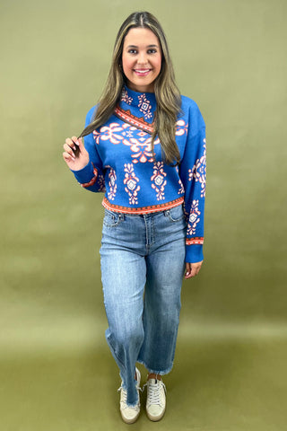 Woman wearing a blue floral sweater and jeans against a green background