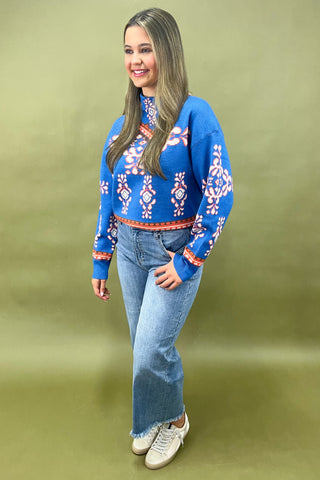 Woman wearing a blue patterned sweater and jeans on a green background