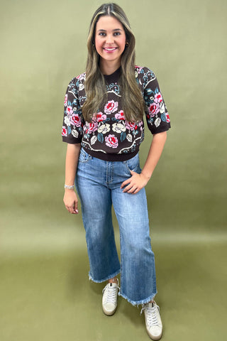 Brown short sleeve knit sweater with colorful floral pattern styled with light wash wide leg jeans and white sneakers