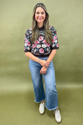 Brown short sleeve knit sweater with colorful floral pattern styled with light wash wide leg jeans and white sneakers