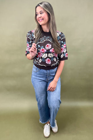 Brown short sleeve knit sweater with colorful floral pattern styled with light wash wide leg jeans and white sneakers