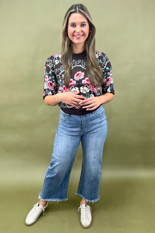 Brown short sleeve knit sweater with colorful floral pattern styled with light wash wide leg jeans and white sneakers