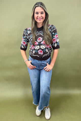 Brown short sleeve knit sweater with colorful floral pattern styled with light wash wide leg jeans and white sneakers