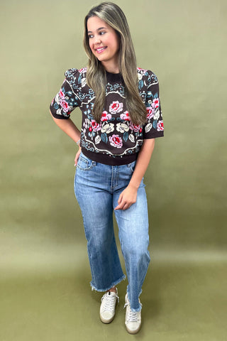 Brown short sleeve knit sweater with colorful floral pattern styled with light wash wide leg jeans and white sneakers