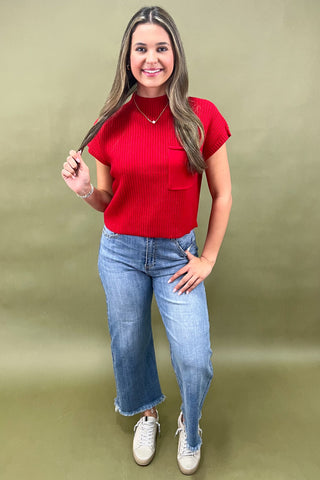Woman wearing a red top and blue jeans against a green background