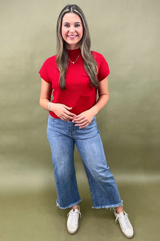 Woman wearing a red top and blue jeans against a green background