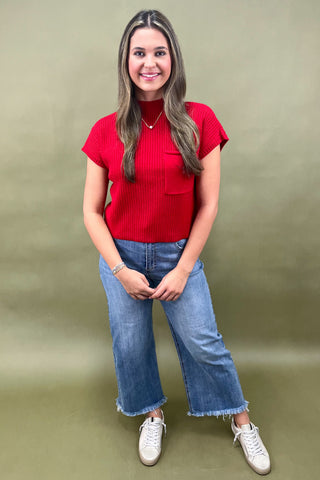Woman wearing a red top and blue jeans against a green background