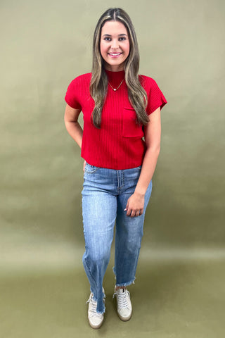 Woman wearing a red top and blue jeans against a green background