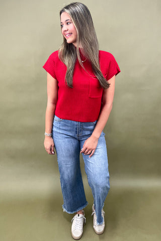 Woman wearing a red top and blue jeans against a green background