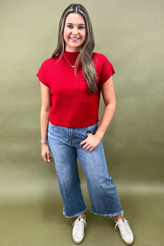 Woman wearing a red top and blue jeans against a green background